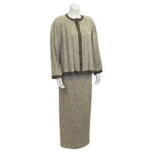 Puede incluir: Un traje de dos piezas en tejido tweed beige y marrón. La chaqueta tiene un escote redondo y cierre de botón. La falda es de línea A y llega a las rodillas.