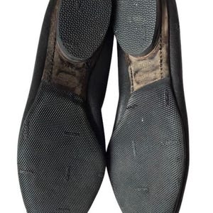 May include: A pair of black shoes shown from the bottom view, featuring textured rubber outsoles with the Vibram logo embossed on the surface. The heels are rounded and the size 36.5 is clearly printed on the inner sole area of the right shoe.