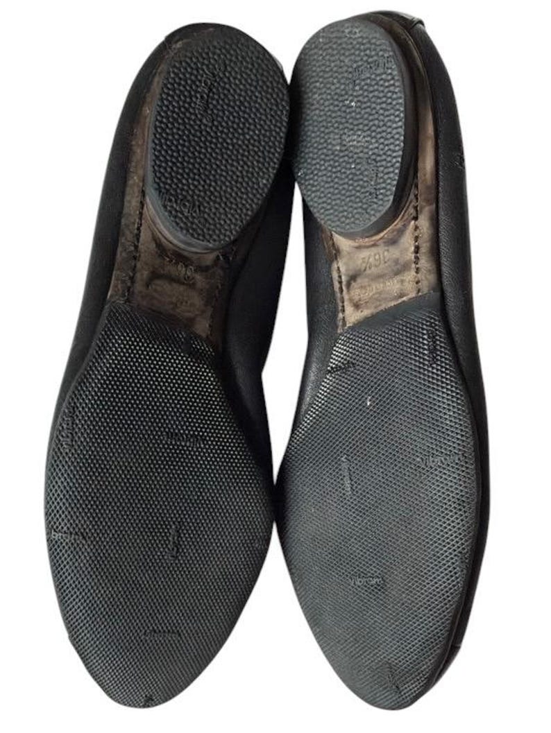 May include: A pair of black shoes shown from the bottom view, featuring textured rubber outsoles with the Vibram logo embossed on the surface. The heels are rounded and the size 36.5 is clearly printed on the inner sole area of the right shoe.