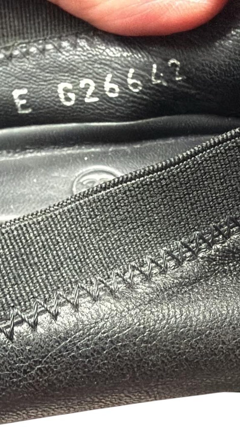 May include: A black leather shoe interior featuring a textured elastic trim with visible zigzag stitching. The inner lining displays the stamped alphanumeric code E 626642 in white ink, along with a faint circular logo embossed on the footbed surface.