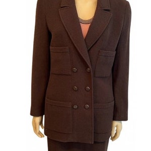 Puede incluir: Un traje de chaqueta y falda marrón de doble botonadura. La chaqueta tiene dos bolsillos grandes con solapa y cuatro botones en la parte delantera. La falda es de largo hasta la rodilla.