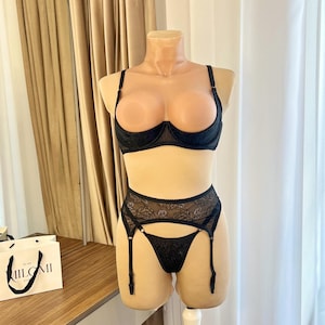 Op de afbeelding: Zwarte lingerie set op een mannequin. De set bestaat uit een bh, jarretelgordel en string. De bh heeft beugel. De jarretelgordel en string zijn gemaakt van kant. De set wordt getoond op een mannequin.