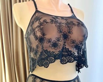 Pode incluir: Conjunto de lingerie de renda floral preta. O conjunto inclui um top curto estilo halter e calcinhas de cintura baixa combinando. A renda delicada apresenta um padrão floral repetido. A lingerie é transparente, com alças ajustáveis na parte superior.