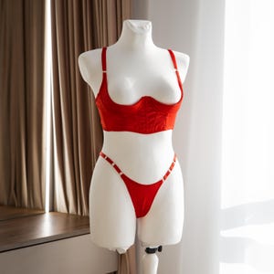 Könnte beinhalten: Rotes Dessous-Set auf einer weißen Schaufensterpuppe. Das Set besteht aus einem Bustier-Top mit verstellbaren Trägern und einem String-Höschen. Das Bustier hat einen Sweetheart-Ausschnitt. Der String hat dünne Träger mit kleinen, dekorativen Akzenten.
