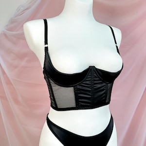 Op de afbeelding: Zwarte satijnen en mesh lingerie top met een corset stijl en een diep decollet&eacute;.