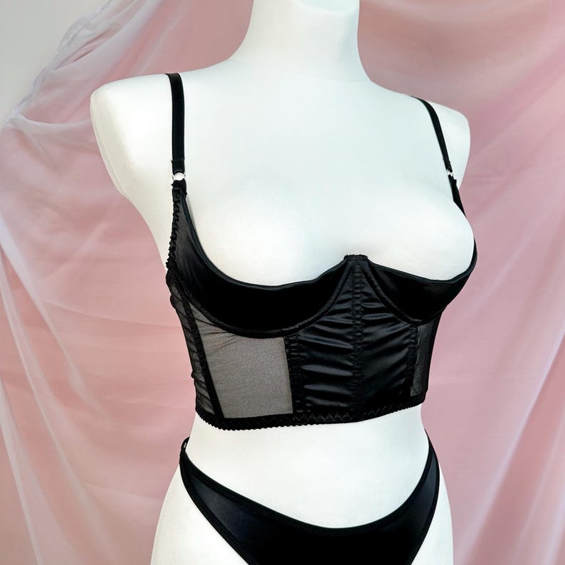Op de afbeelding: Zwarte satijnen en mesh lingerie top met een corset stijl en een diep decollet&eacute;.
