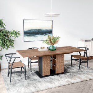May include: A wooden dining table with a black metal base and a shelf. The table is set with four black chairs with woven seats. A vase with dried flowers sits on the table, and a painting hangs on the wall behind the table.