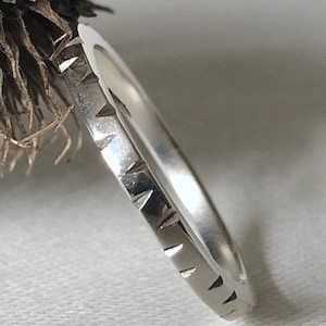 Puede incluir: Un anillo de plata con una banda texturizada que presenta un patrón triangular repetitivo.