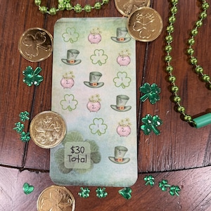 May include: A St. Patrick's Day-themed arrangement featuring gold coins with shamrock designs, green shamrock-shaped decorations, and a green beaded necklace. A card with leprechaun hats and shamrocks is also present. The card reads "$30 Total".