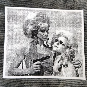 May include: Black and white sticker featuring a retro illustration of two figures. One figure holds a gun, while the other wears sunglasses and has a skull-like face. The image has a grainy, vintage aesthetic.