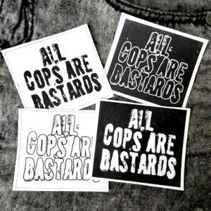 Peut inclure: Quatre autocollants carrés avec le texte "ALL COPS ARE BASTARDS" en gras, police sans-serif. Deux autocollants ont un fond noir avec du texte blanc, et deux ont un fond blanc avec du texte noir.