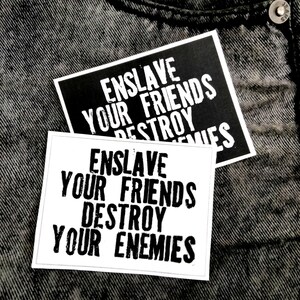 May include: Two rectangular stickers with white text on a black background and black text on a white background. Both stickers feature the bold, distressed-style lettering: ENSLAVE YOUR FRIENDS DESTROY YOUR ENEMIES. The stickers are layered on top of each other.