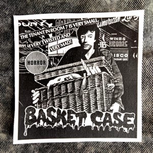 Peut inclure: Autocollant noir et blanc avec un homme tenant un panier en osier. Le texte "BASKET CASE" est en police dégoulinante, avec "HORROR" et "THE TENANT IN ROOM 7 IS VERY SMALL, VERY TWISTED AND VERY MAD!".