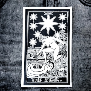 May include: A rectangular black and white patch featuring a tarot card illustration titled THE STAR. The design depicts a figure kneeling by a pool of water, pouring liquid from a vessel, surrounded by eight stars and the Roman numeral XVII.