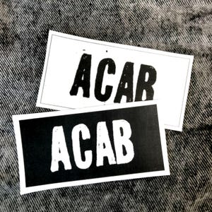 Peut inclure: Deux autocollants noir et blanc avec le texte "ACAB" imprimé dessus. Les autocollants sont sur un fond en jean.
