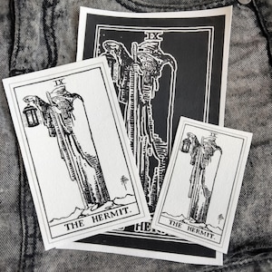 May include: Three rectangular prints featuring a black and white illustration of The Hermit tarot card, marked with the Roman numeral IX. Each print depicts a robed figure holding a lantern and a staff, with the text THE HERMIT printed at the bottom.