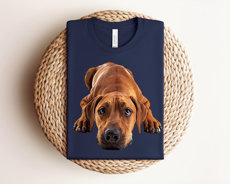May include: A navy blue t-shirt featuring a graphic illustration of a brown dog lying down with its head facing forward. The dog has large, expressive eyes and a black nose. The shirt has a crew neckline and a white brand label at the collar.
