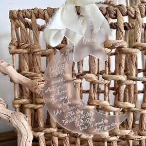 May include: A clear acrylic crescent moon and star ornament with the text "Twinkle Twinkle little star how I wonder what you are up above the world so high like a diamond in the sky Twinkle Twinkle little star how I wonder what you are" and the name "Luca" on the star.