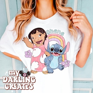 K&ouml;nnte beinhalten: Wei&szlig;es T-Shirt mit einem rosa und blauen Cartoon-Bild von Lilo und Stitch. Das Bild enth&auml;lt einen Regenbogen und das Wort "Ohana".