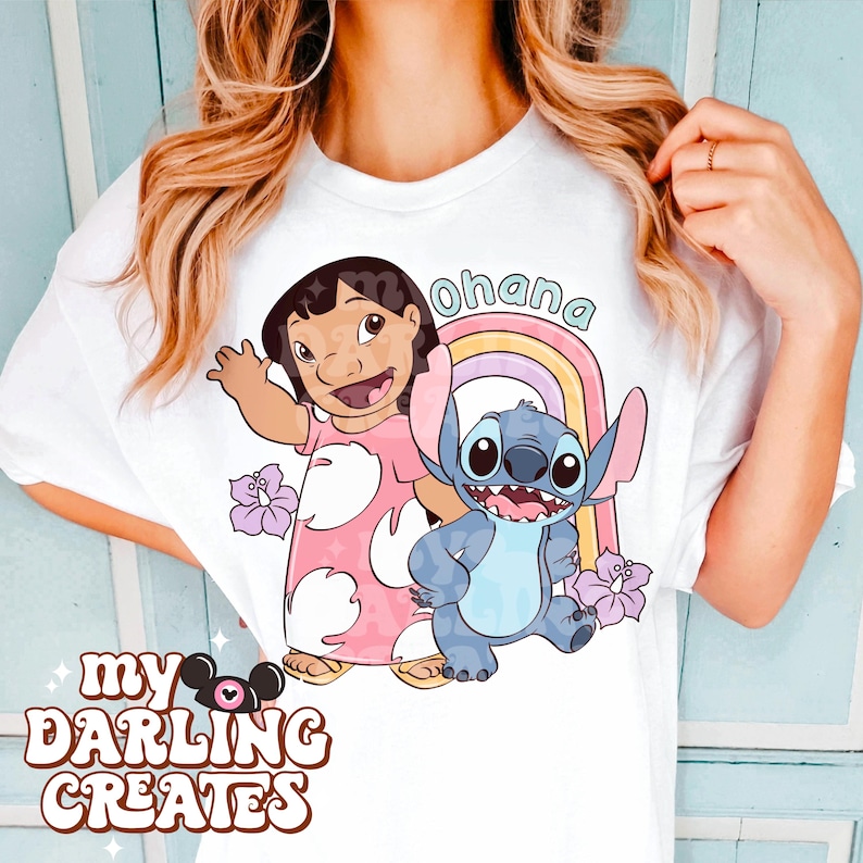 K&ouml;nnte beinhalten: Wei&szlig;es T-Shirt mit einem rosa und blauen Cartoon-Bild von Lilo und Stitch. Das Bild enth&auml;lt einen Regenbogen und das Wort "Ohana".