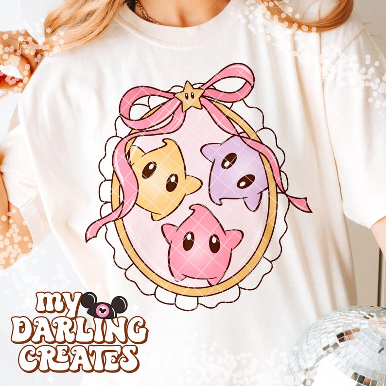 Puede incluir: Sudadera color crema con un dise&ntilde;o caprichoso de tres personajes en forma de estrella en amarillo, morado y rosa, dentro de un marco decorativo con un lazo rosa. El texto "my DARLING CREATES" est&aacute; impreso en la parte inferior.