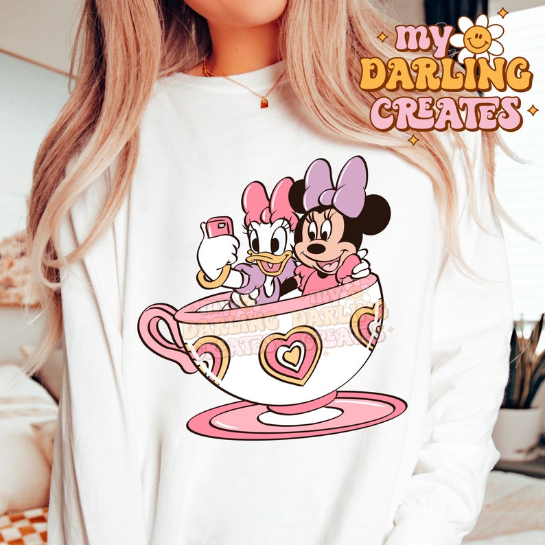 May include: White sweatshirt with a pink teacup design featuring Disney's Minnie Mouse and Daisy Duck. The text "my darling creates" is printed in pink and yellow on the top right corner of the sweatshirt.