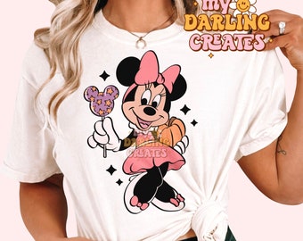 May include: White t-shirt with a cartoon image of Minnie Mouse holding a purple and yellow lollipop and a pumpkin. The text "my darling creates" is in the top right corner of the image.
