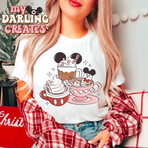 May include: White t-shirt featuring a whimsical design of three Mickey Mouse-themed hot beverages. The design includes a coffee, a whipped cream drink, and a pink teacup with marshmallows. The shirt has the text "my DARLING CREATES" in a retro font.