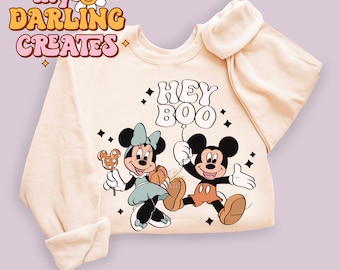 May include: A beige sweatshirt with a graphic of Mickey Mouse and Minnie Mouse holding a balloon that says "Hey Boo".