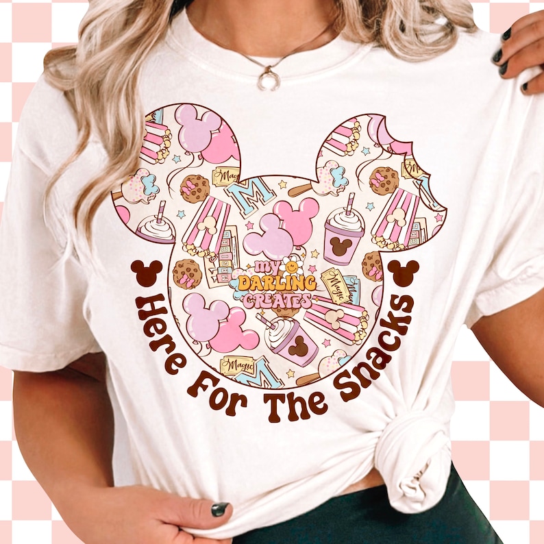 May include: White t-shirt featuring a pink and brown Mickey Mouse head design. The design is filled with various images of snacks, including popcorn, ice cream, and Mickey Mouse ears. The text "Here For The Snacks" is written below the Mickey Mouse head.