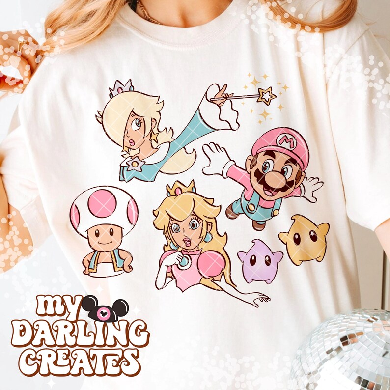 May include: Cream-colored t-shirt featuring cartoon characters from a popular video game. The design includes Mario, Princess Peach, Rosalina, Toad, and other characters. The text "MY DARLING CREATES" is printed at the bottom of the design.