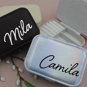 Puede incluir: Tres pequeñas cajas de joyería con diferentes colores y acabados. Las cajas están personalizadas con los nombres "Mila" y "Camila" en una fuente cursiva.