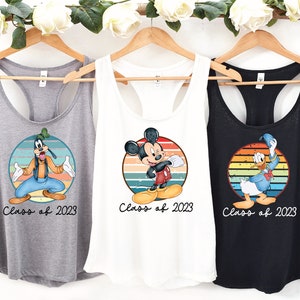 May include: Three tank tops with a retro-style design featuring Mickey Mouse, Donald Duck, and Goofy. Each tank top has a colorful striped circle with the character in the center. The text "Class of 2023" is printed below each character.