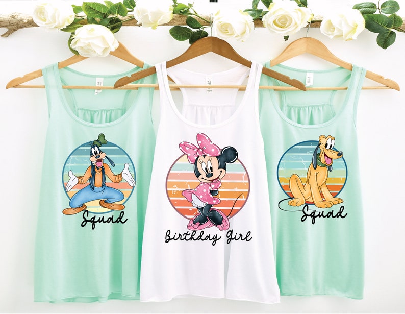 May include: Three mint green tank tops with a retro-style graphic of Disney characters. The center tank top is white and features Minnie Mouse with the text "Birthday Girl". The left and right tank tops feature Goofy and Pluto, respectively, with the text "Squad".