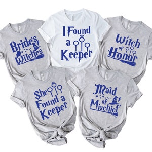 May include: Five t-shirts with blue text on a white or gray background. The shirts have phrases like "Brides Witches", "I Found a Keeper", "Witch of Honor", "She Found a Keeper", and "Maid of Mischief". The shirts are likely for a bridal party.