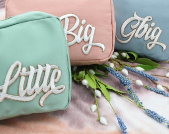 Puede incluir: Tres bolsas de tela con letras bordadas. Las bolsas son en tonos de rosa, azul y verde. Las letras dicen "Big", "Gbig" y "Little".