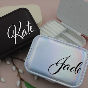 Puede incluir: Dos pequeñas cajas de joyería con nombres personalizados. La caja de la izquierda es negra con el nombre "Kate" en letras blancas. La caja de la derecha es plateada con un acabado holográfico y el nombre "Jade" en letras negras.