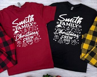 Può includere: Due magliette, una bordeaux e una nera, con la scritta "Smith Family Christmas Crew 2025" in bianco. Il design include fiocchi di neve, un cappello di Babbo Natale, un omino di pan di zenzero e altri elementi festivi. Sono visibili pantaloni del pigiama a quadri.