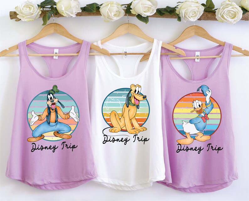 May include: Three purple, white, and light purple tank tops with a retro rainbow design and a Disney character on each. The tank tops say "Disney Trip" on the bottom. The characters are Goofy, Pluto, and Donald Duck.