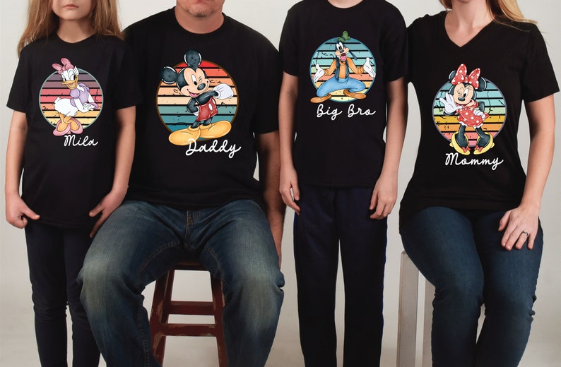May include: A set of four black t-shirts with a vintage-style design featuring Disney characters. The shirts have the text "Daddy", "Mammy", "Big Bro", and "Mila" printed on them.