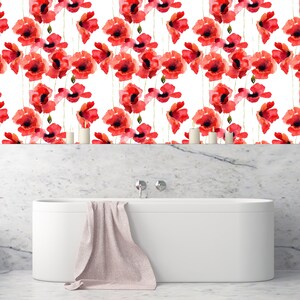 May include: A white bathtub with a pink towel on the edge. The bathtub is in front of a white marble wall with a red poppy floral pattern wallpaper.