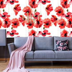 May include: A gray sofa with a pink throw blanket and a floral patterned pillow in front of a white wall with a red poppy flower pattern.