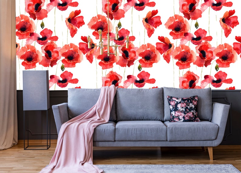 May include: A gray sofa with a pink throw blanket and a floral patterned pillow in front of a white wall with a red poppy flower pattern.