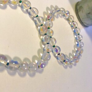 May include: Two iridescent clear glass bead bracelets with green string accents.