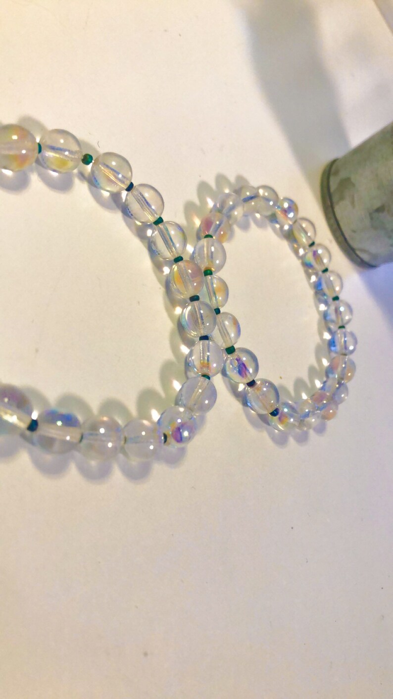 May include: Two iridescent clear glass bead bracelets with green string accents.