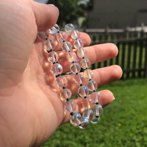 May include: A strand of iridescent clear glass beads with black string.