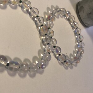 May include: Two iridescent clear glass bead bracelets with black string between each bead.