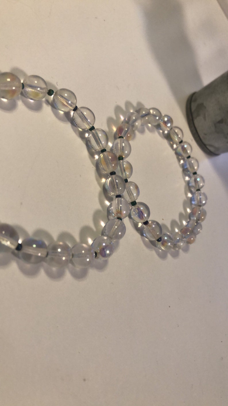 May include: Two iridescent clear glass bead bracelets with black string between each bead.