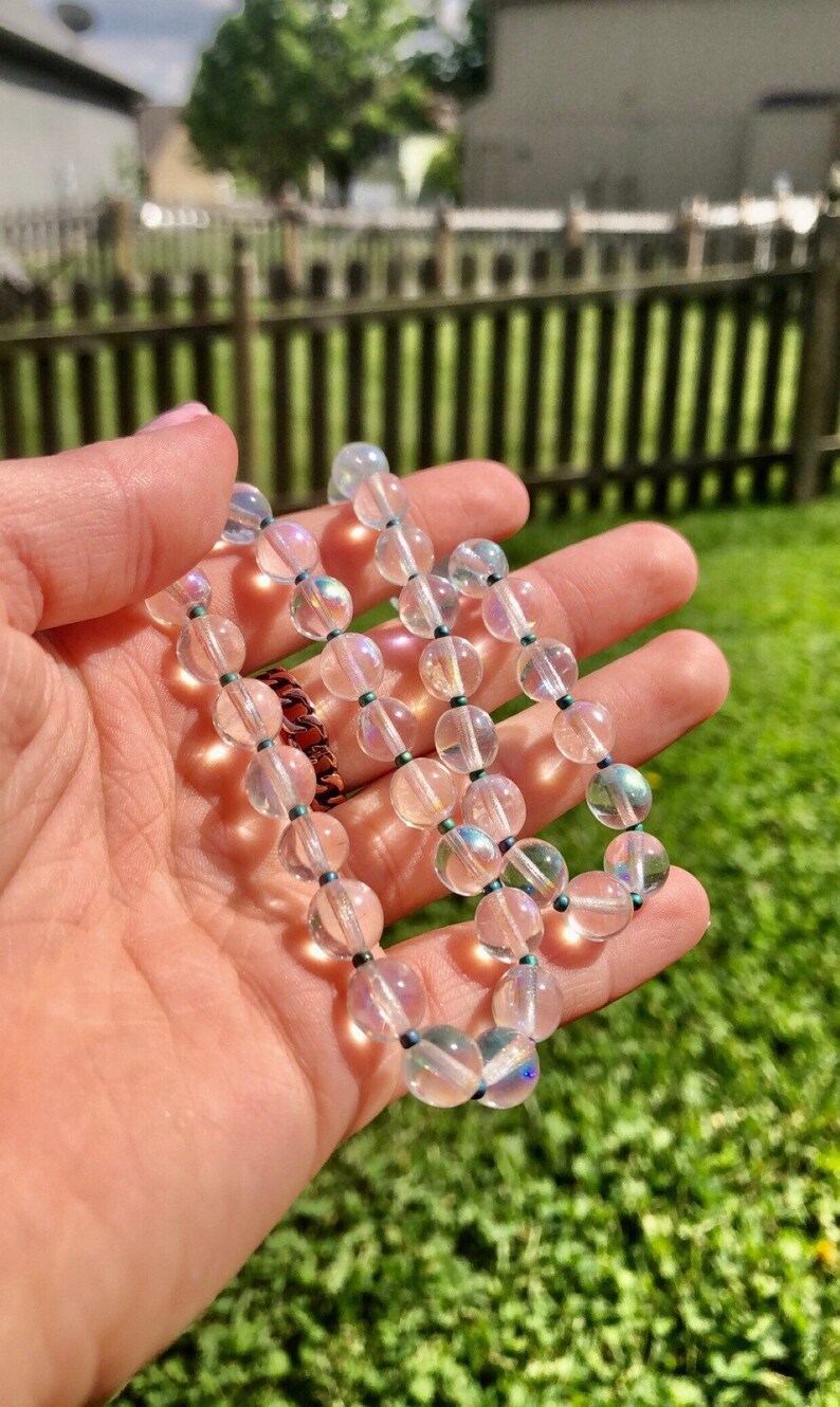 May include: A white iridescent crystal beaded necklace with dark blue beads between each crystal bead.