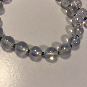 May include: A strand of iridescent clear glass beads with dark green spacers. The beads are round and have a slight shimmer.